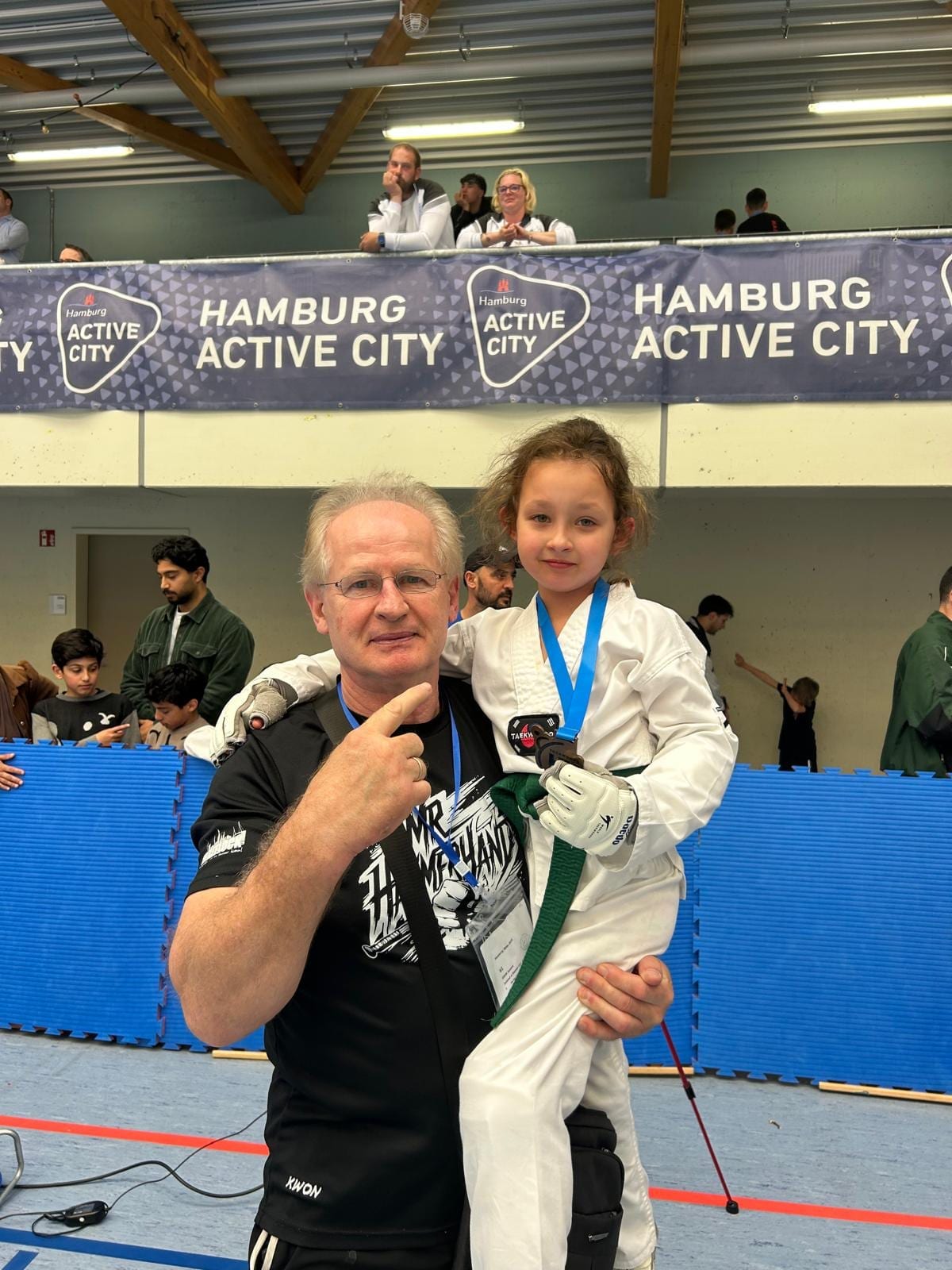 Trainer und ein Kind mit Medaille vor einer Turnierhalle