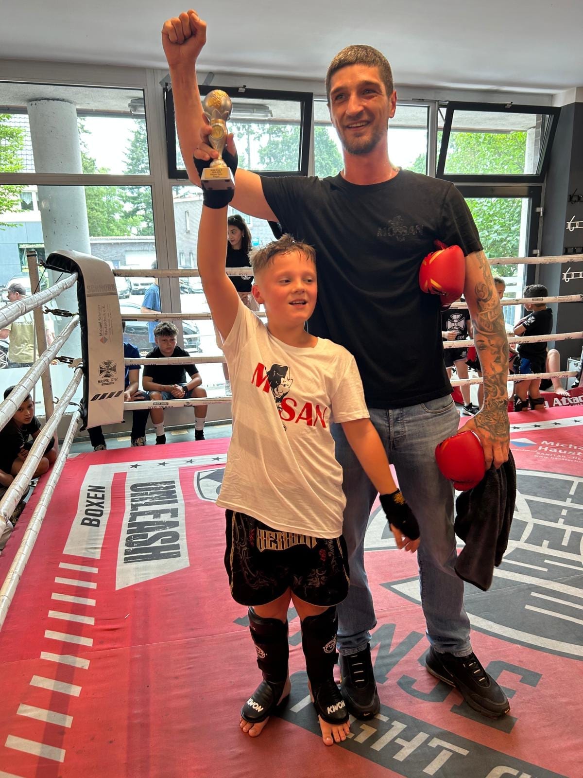 Trainer hebt im Ring den Arm eines Jungen nach gewonnenem Kampf
